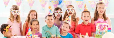 Large group of children celebrating a little boy's birthday with decorations, party hats, and a cake.