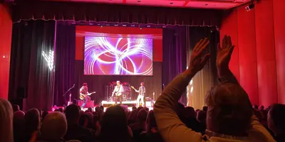 Band on stage while someone in the foreground claps with their hands above their head