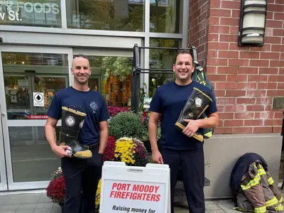 Two off duty firefighters holding a boot in front of a sign