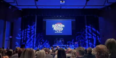 Illuminated stage with Bad Moon Rising sign, concert goers sit in their seats