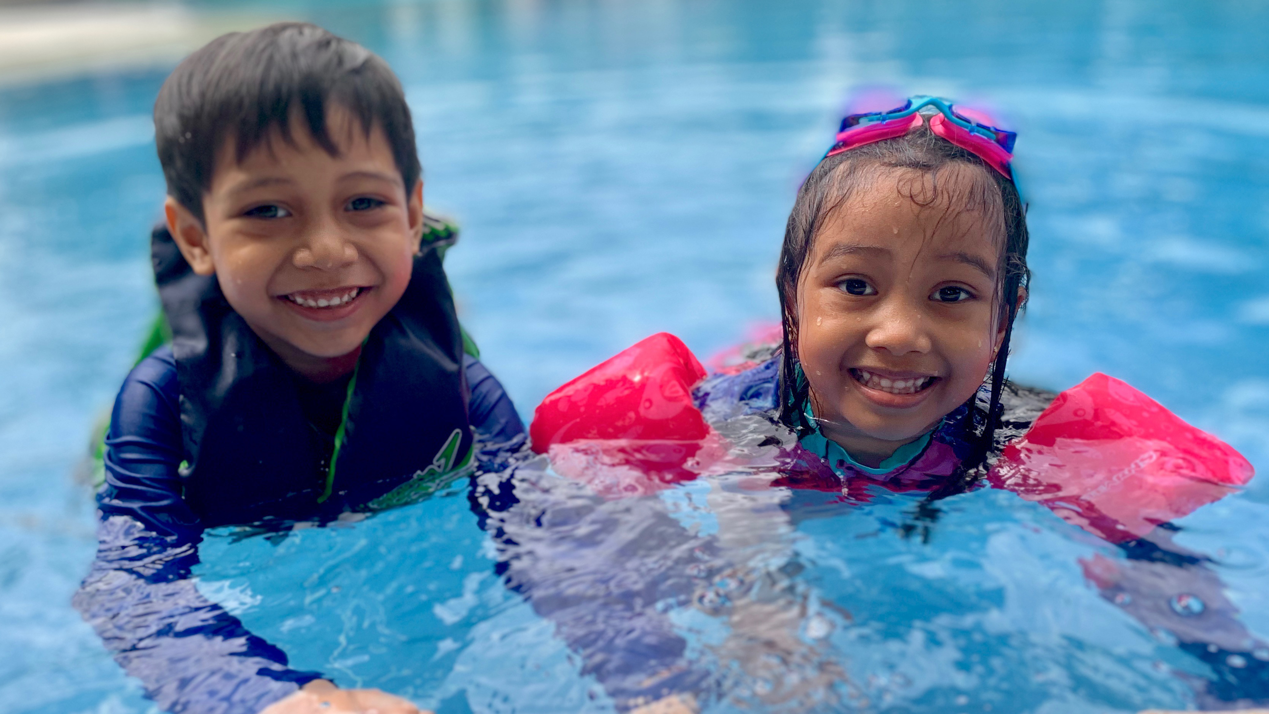Two kids wearing goggles in a swimming pool