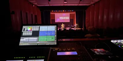 A band on stage with the booth window and monitor in the foreground